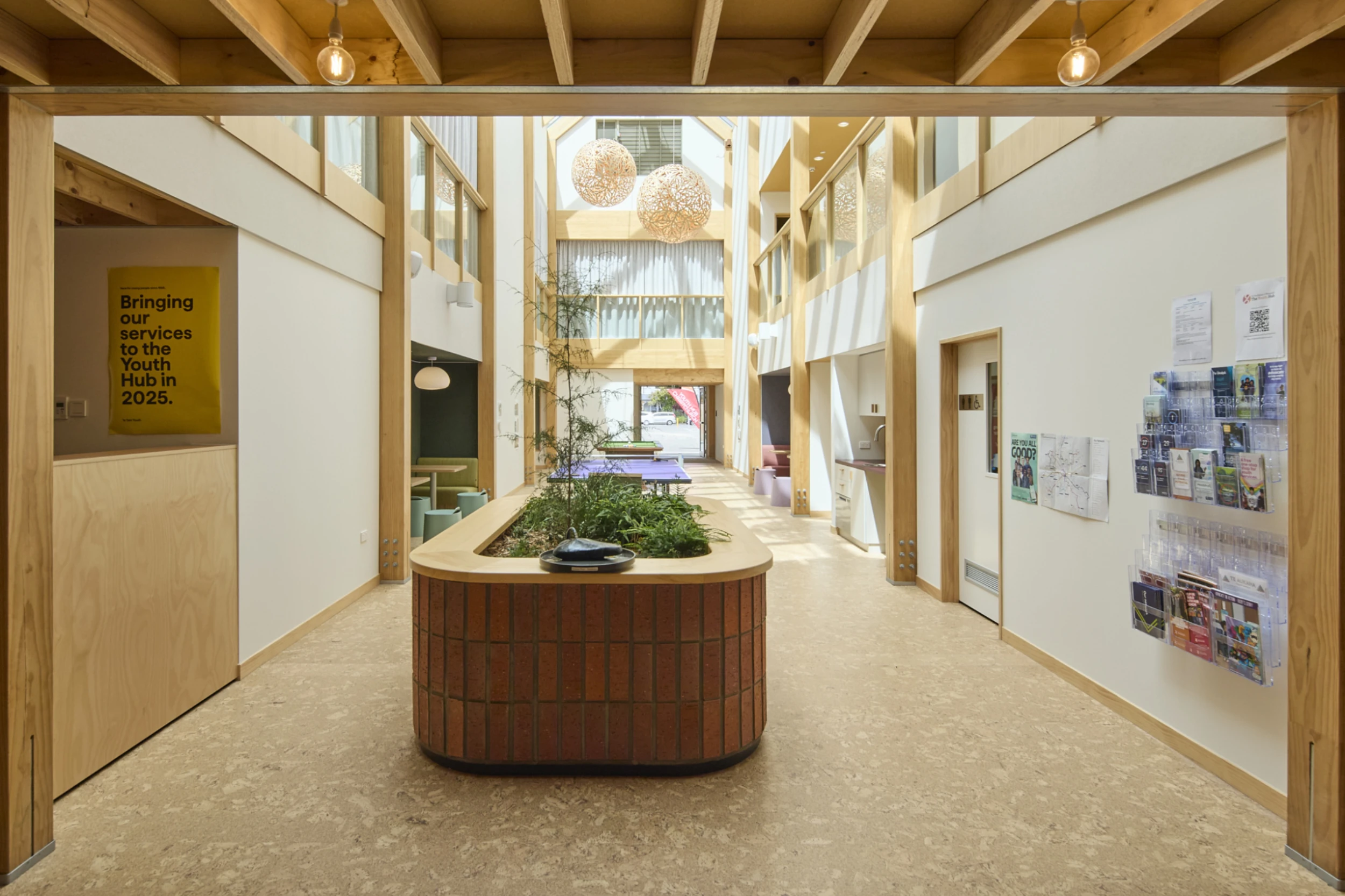 Spacious, modern lobby with wooden accents, a central planter, and natural light. Posters and brochures line one wall, creating an inviting atmosphere.